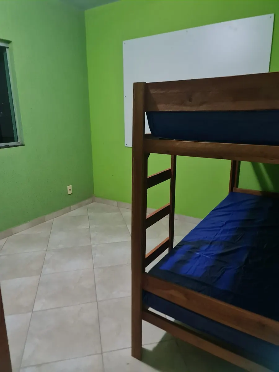 Dormitório de paredes verdes com beliche de madeira, quadro branco e piso claro